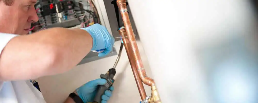 Water heater repair technician testing copper pipe connections and controls in Overland Park, KS